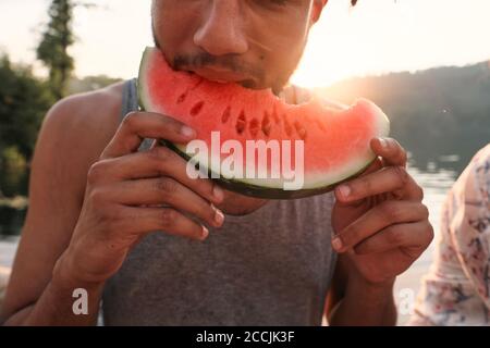 Nahaufnahme eines jungen Mannes, der beim Picknick im Freien Wassermelone beißt Stockfoto