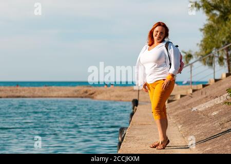 Der Sommer und die Feiertage. Eine glückliche übergewichtige Frau posiert auf einem Seebrücke. Stockfoto