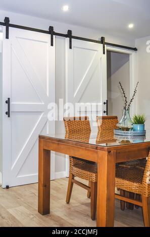 Selektive Konzentration auf ein helles Esszimmer mit einem Holztisch und Rattanstühlen. Weiße Schiebetüren im Hintergrund. Stockfoto