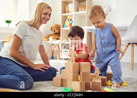 Mutter und Sohn bauen im Zimmer einen Turm aus Holzwürfeln. Mutter unterrichtet Kinder am Tag der Auszeit zu Hause Stockfoto