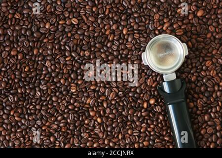 Draufsicht auf viele geröstete aromatische Kaffeebohnen, auf denen der Halter Filter aus der Kaffeemaschine liegt. Hintergrund Kaffeebohne. Ein belebender Körper Stockfoto