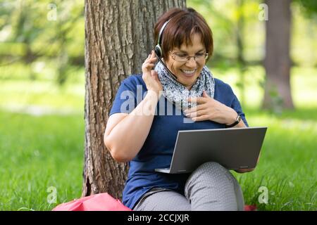 Eine Frau mittleren Alters, die ihren Laptop und ihr Headset benutzt - spricht mit ihren Freunden und ihrer Familie. Online-Anruf. Stockfoto
