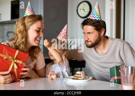 Glückliche Familie gratulieren Tochter Geburtstag in der Küche, geben sie Geschenke an sie, feiern. Familie zu Hause Stockfoto