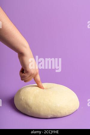 Sauerteig isoliert auf einem lila nahtlosen Hintergrund. Frau prüft Teig. Hausbackkonzept. Bereit, rohen Teig zu backen. Brotgebäck machen. Stockfoto