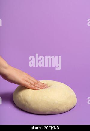 Frau testet den Teig, isoliert auf einem nahtlosen violetten Hintergrund. Brotbacken Konzept. Handgemachter Sauerteig. Brot zu Hause machen. Pizzateig. Stockfoto