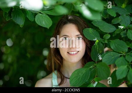 Nahaufnahme einer lächelnden jungen Frau von Pflanzen im Wald Stockfoto