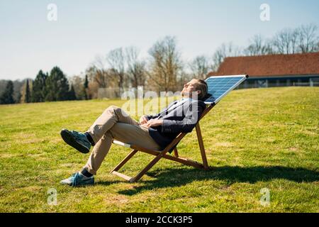 Geschäftsmann entspannen auf Stuhl mit Solarpanel im Park während Sonniger Tag Stockfoto