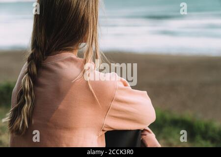 Nahaufnahme einer jungen Frau mit geflochtenen Haaren, die am Strand sitzt Bei Sonnenuntergang Stockfoto