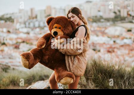 Junge Frau umarmt Teddybär, während Stadt im Hintergrund Stockfoto