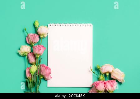 Leeres Notizbuch mit rosa Blüten auf grünem Hintergrund, Mockup Stockfoto