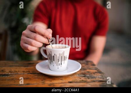 Nahaufnahme von Menschenhand, die Kaffee rührt, während man auf dem Bürgersteig sitzt Café Stockfoto