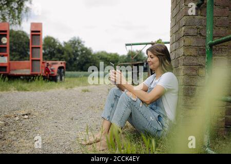 Junge Frau mit Tablette auf einem Bauernhof sitzen an einem Ziegelwand Stockfoto