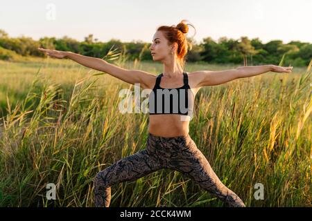 Frau übt Krieger zwei Yoga-Pose auf Gras Feld Stockfoto