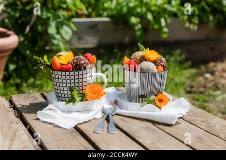 Dessert mit Energiebällchen (rohe Süßwaren) und frischen Früchten und Blumen im Garten Tabelle Stockfoto