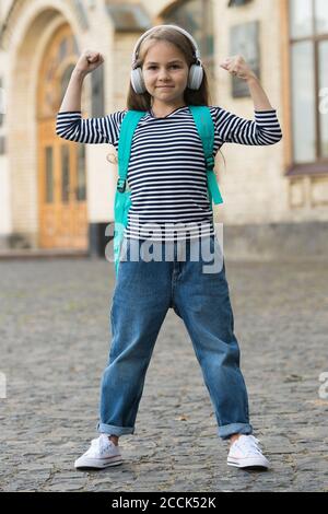 Schönheit gibt Kraft. Kleine Kinder Flex Arme im Freien. Mädchenleistung. Kleines Kind hört Musik in Kopfhörern. Musik ist Macht. Neue Technologie. Modernes Leben. Lässiger Style. Modisches Outfit. Stockfoto