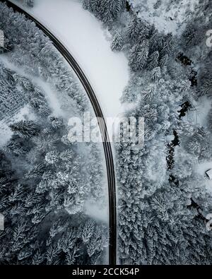 Luftaufnahme der leeren Asphaltstraße, die durch schneebedeckten Wald schneidet In Achtal Stockfoto