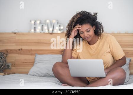 Junge Frau mit lockigen Haaren mit Laptop, während sie sitzt Bett Stockfoto