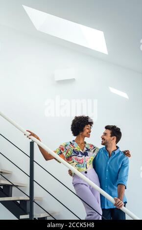 Zärtliches multiethnisches Paar, das auf schwimmenden Treppen in einem modernen Penthouse steht Stockfoto