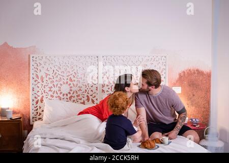 Eltern küssen beim Frühstück mit Sohn Bett zu Hause Stockfoto