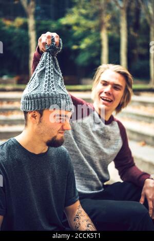 Männlich Entfernen Freund Strickmütze, während im öffentlichen Park sitzen Stockfoto