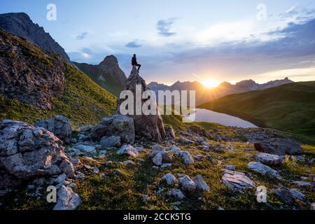 Wanderer, der bei Sonnenuntergang am Rappensee, Bayern, auf Felsen sitzt Stockfoto