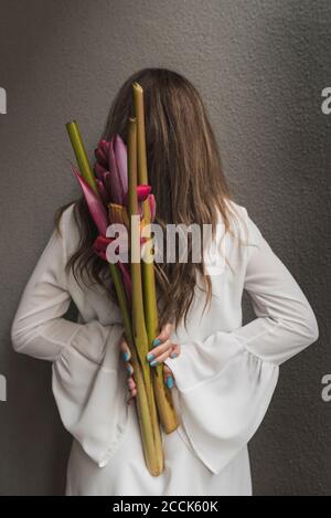 Frau mit braunem Haar hält Bouquet hinter Rücken an Wand Stockfoto