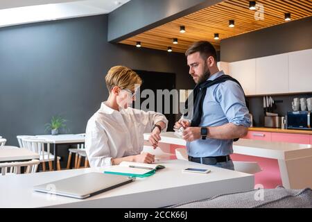 Besorgt Geschäftsfrau Überprüfung der Zeit, während von Geschäftsmann auf kreative stehen Coworking Office Stockfoto