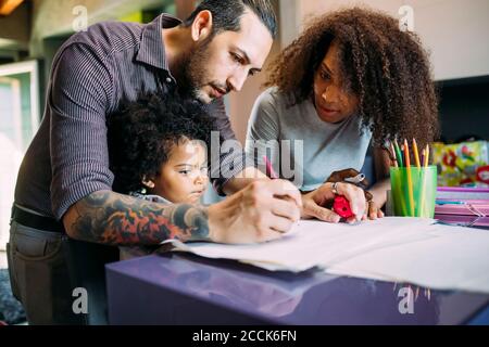 Frau, die den Vater mit der Tochter anschaut, die auf Papier zeichnet Zu Hause Stockfoto
