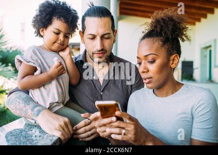 Frau zeigt dem Mann und der Tochter auf dem Balkon ein Smartphone Stockfoto