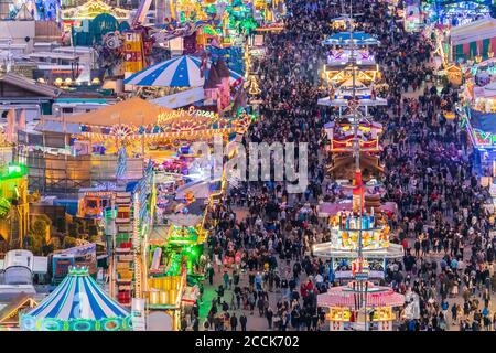 Deutschland, Bayern, München, Drohne Blick auf Menschenmassen, die das Oktoberfest in einem riesigen Vergnügungspark in der Abenddämmerung feiern Stockfoto