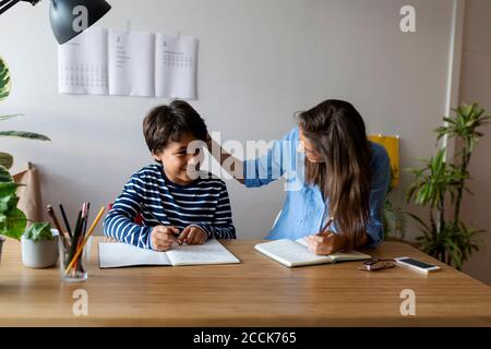 Tutorin im Gespräch mit lächelndem Jungen, während sie am Tisch sitzt Stockfoto