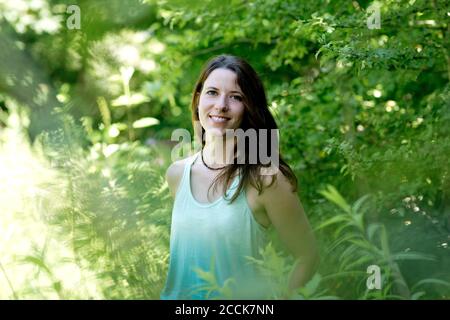 Lächelnde junge Frau, die inmitten von Pflanzen im Wald steht Stockfoto