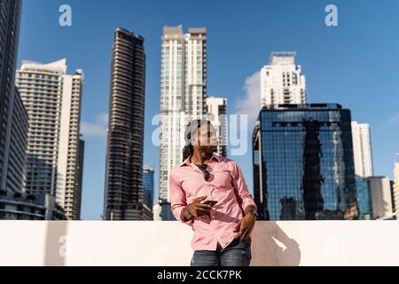 Nachdenklicher Afro-Mann hält Smartphone steht gegen Wolkenkratzer in Miami, Florida, USA Stockfoto