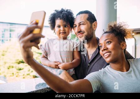 Lächelnde Frau beim Selfie mit Vater und Tochter auf dem Balkon Stockfoto