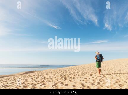 Senior Mann mit Rucksack Blick auf den Atlantik, während Sie am Strand stehen, Düne von Pilat, Nouvelle-Aquitaine, Frankreich Stockfoto