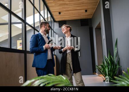Lächelnde Kollegen sprechen, während sie im Büroflur stehen Pause Stockfoto