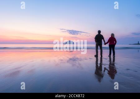 Paar blickt auf das Meer, während sie am Seacliff Beach, North Berwick, Schottland während des Sonnenuntergangs stehen Stockfoto