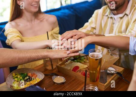 kaukasische Gruppe der besten Freunde zusammengeschlossen Hände sitzen am Café-Tisch, glückliche junge Menschen in der Begegnung, Einheit und Unterstützung. Freundschaftskonzept Stockfoto