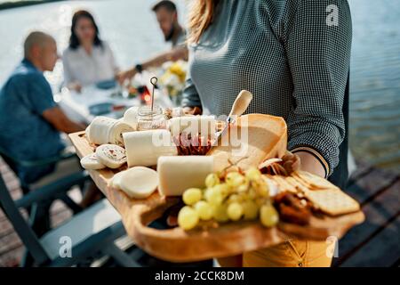 Freunde, die mit einer Käseplatte an einem See zu Abend essen Stockfoto