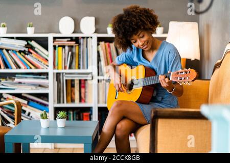Glückliche Frau spielt Gitarre, während sie auf dem Sofa im Kaffee sitzt Kaufen Stockfoto