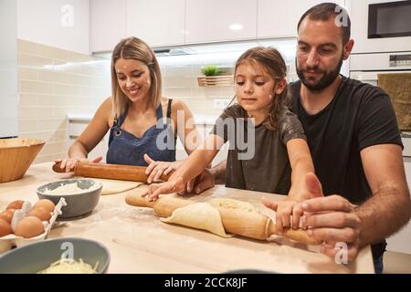 Eltern mit Tochter kneten Pizzateig auf dem Tisch in der Küche Stockfoto