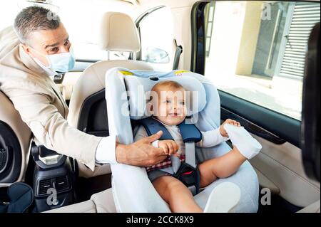 Vater trägt Schutzmaske Baby Junge sitzt auf Kindersitz In einem Auto Stockfoto