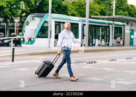Geschäftsmann mit Gepäck auf Rädern über die Straße in der Stadt Stockfoto