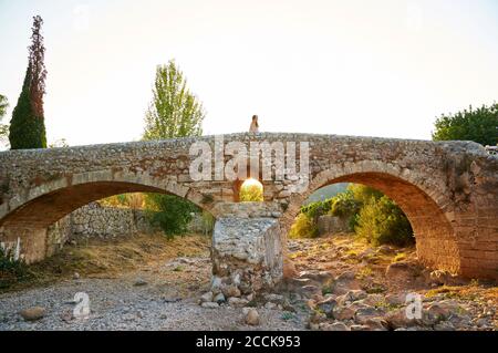 Frau auf der Puente Romano, einer römischen Brücke aus dem 19. Jahrhundert über Torrent de Sant Jordi in Pollença bei Sonnenuntergang (Pollensa, Mallorca, Balearen, Spanien) Stockfoto