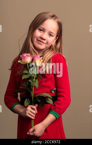 Junge hübsche 8-jährige Mädchen trägt ein rotes Kleid Halten Blumen isoliert auf orange farbigen Hintergrund Stockfoto