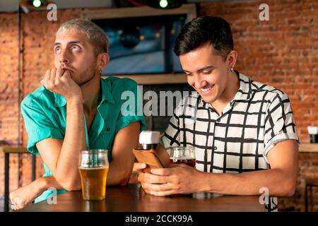 Gelangweilt Gay Mann sitzend von Partner mit Handy bei Bar Stockfoto