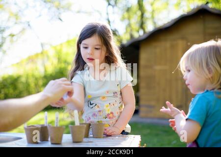 Vater gibt Samen für Mädchen, während im Garten auf dem Tisch bei Hof Stockfoto