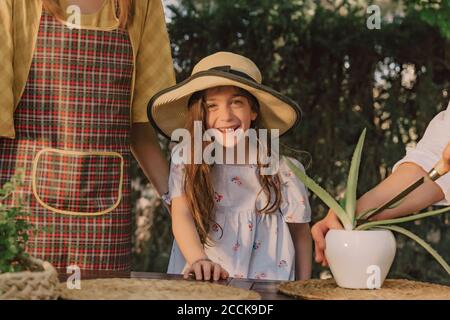 Lächelndes Mädchen mit Hut, das mit Mutter und Großmutter steht Tisch im Hof Stockfoto