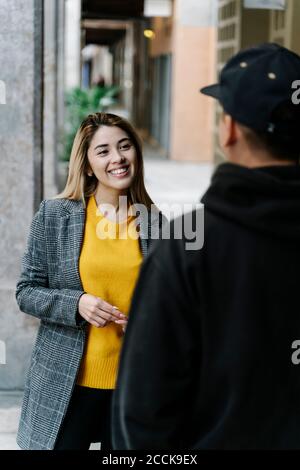 Junge lächelnde Frau während der Begegnung mit jungen Mann in der Stadt