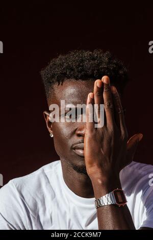 Nahaufnahme eines afrikanischen jungen Mannes, der das Gesicht mit der Hand bedeckt Stockfoto